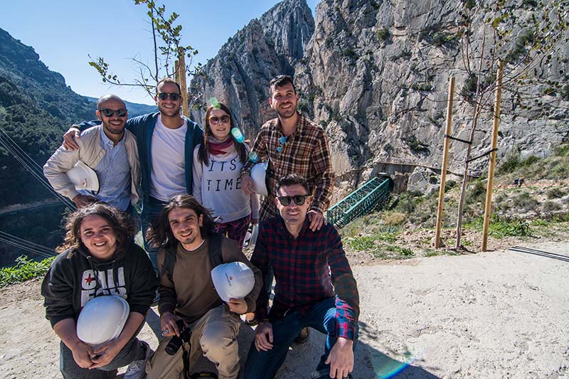 Un grupo de amigos sonríen y posan para la cámara en el Caminito del Rey. Se observan de fondo puentes colgantes y un paisaje montañoso.