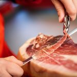 professional-cutter-carving-slices-from-whole-bone-in-serrano-ham-min